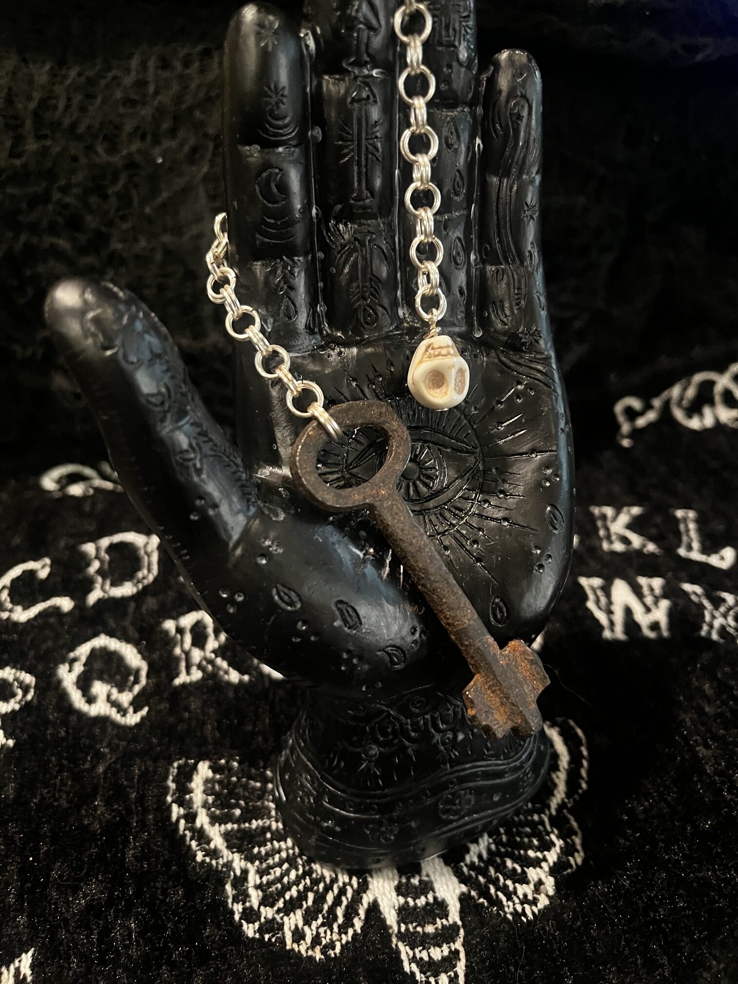 Skeleton key pendulum displayed on palmistry hand with ouija background
